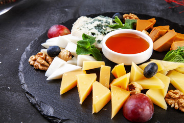 Close up on cheese plate served with nuts, grapes, honey. View from above on different types of cheese on dark background with copy space