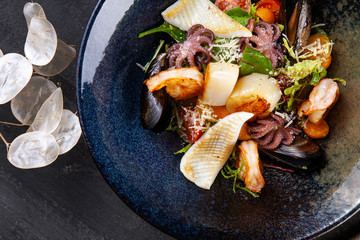 Close up on seafood salad with squid, shrimp, scallops, mussels, baby octopus, cherry tomato and greens. Salad bowl served on restaurant table. Top view food. Copy space