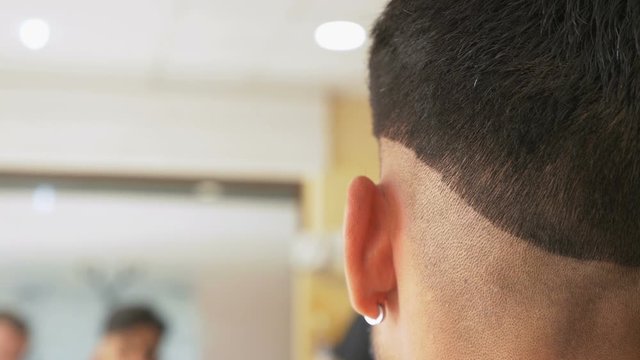 Professional barber makes a trendy haircut to client, hairstyling process in barbershop. Hairstylist trims hair of customer with hair clipper at salon. Hairdresser serving client with at salon.
