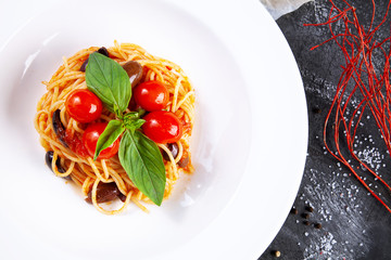 Top view on traditional italian pasta with basil and cherry tomato in white plate. Flat lay italian cuisine with copy space for design. mediterranean noodle for lunch. Dark background