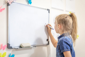 Little girl writing on empty whiteboard with a marker pen. Learning, education and back to school concept with copy space