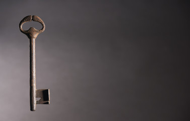Old key to the left of the page. Secret and protection concept. Isolated on dark background. Copy...