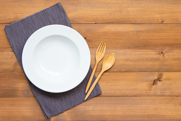 Empty white circle plate with spoon and fork on wooden table. Top view