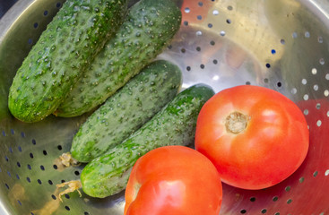 Tomatoes with cucumbers in a metal bowl of colander