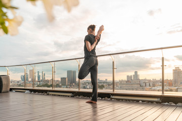 Attractive handsome athletic man practicing yoga in business center with beautiful view on a city from skyscraper