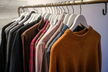 Obraz premium Clothes in the forms of sweaters and shirts of different textile fabrics and colors are haning on hangers on a clothing rack in a bedroom