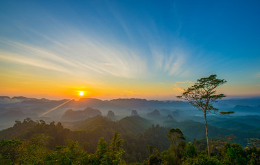 Beautiful mountain range with sky blue and orange light of the sun through the clouds in the morning, Background sky during Sunrise with fog on mountain, Abundant lush forest-Image