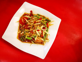 Thai spicy papaya salad, Green papaya salad spicy thai food with white plate on red background, Very famous food in Thailand, Thai food with herbs and spices ingredients, isolated on white background.
