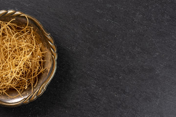 Lot of pieces of thin raw pasta noodles copyspace on right in old iron bowl flatlay on grey stone