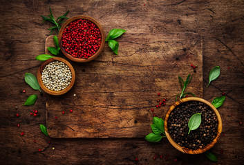 Black, white and pink rose peppers in bowls, assorted spices and spicy herbs on wooden rustic kitchen table, copy space, top view