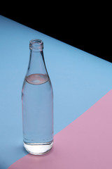 Glass bottle water on a bright pink and blue background close up