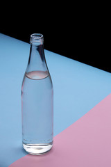 Glass bottle water on a bright pink and blue background close up