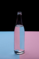 Glass bottle water on a bright pink and blue background close up