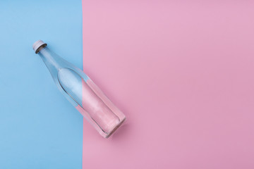 Glass bottle water on a bright pink and blue background close up