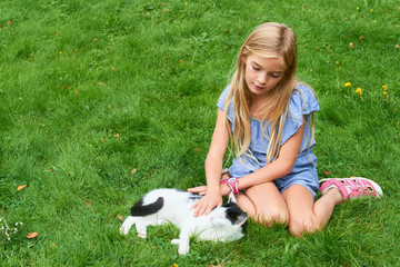 Child blond girl playing and stroking with cat on grass at summer