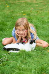 Child blond girl playing and stroking with cat on grass at summer