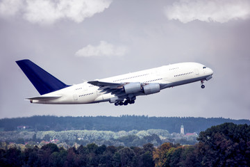 Big jet taking off in blue cloudy sky over the forest.
