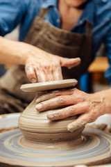 Senior female potter working on pottery wheel while sitting  in her workshop
