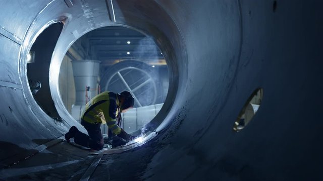 Professional Heavy Industry Welder Working Inside Pipe, Wears Helmet and Starts Welding. Construction of the Oil, Natural Gas and Fuels Transport Pipeline. Industrial Manufacturing Factory