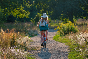 Cyclist with a hat from behind, a woman on a bicycle drives along a path in a meadow