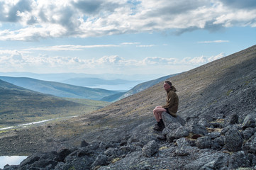 Contemplative man hiker sitting on stone of mountain peak at early morning, seen pleasant outlook over mountains