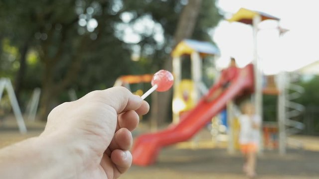 Stranger on the playground offers candy to child. Kids in danger. Suspicious adult man spying on kids and calls a child to himself. Children safety protection, kidnapping concept. First-person view.