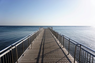 Empty old wooden pier over blue sea with clear cloudless sky background at day time.