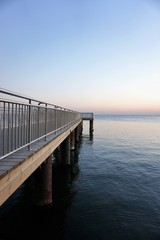 Vertical view of empty wooden pier over blue sea with clear cloudless sky background at sunset.