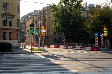 Obraz premium repair of a city road on an early sunny morning at an empty intersection in a residential area with old architecture. working traffic lights and fences in pedestrian areas