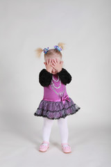 Two years little girl in the pink dress closed her face with her hands in studio