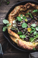 Savory dutch baby pancake with mushrooms and cress micro greens in cast iron skillet on the wooden...