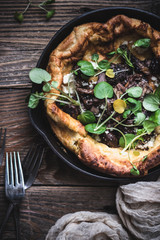 Savory dutch baby pancake with mushrooms and cress micro greens in cast iron skillet on the wooden table