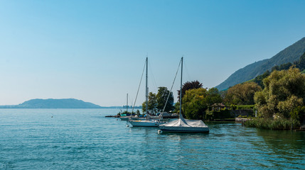 Murtensee Segelboot in der Schweiz mit Bergen und Bäumen im Hintergrund ohne Segel am Mast blauer himmel