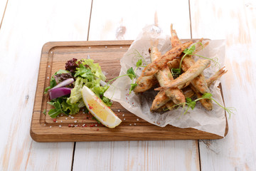 wooden board with smelt fried fish and salad