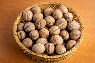 Walnuts in a wooden round bowl on a wooden table in soft focus, brown monochrome photo