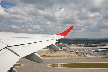 The wing of a take-off airplane. Below is the airport.