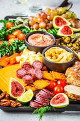 Meat and cheese appetizer platter. Sausage, cheese, hummus, vegetables, fruits and bread on black tray.