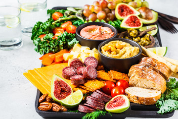 Meat and cheese appetizer platter. Sausage, cheese, hummus, vegetables, fruits and bread on black tray.