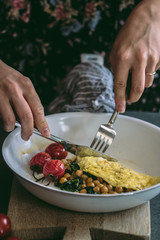 Yellow omelette with chick peas, spinach, cheese and roasted heirloom cherry tomatoes in white frying pan