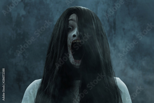 Scary ghost woman screaming on dark background