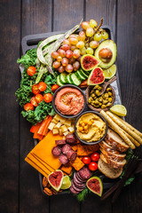 Meat and cheese appetizer platter. Sausage, cheese, hummus, vegetables, fruits and bread on black tray.