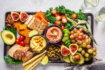Vegan appetizer platter. Hummus, tofu, vegetables, fruits and bread on black tray. - obrazy, fototapety, plakaty