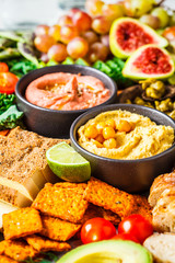 Fototapeta na wymiar Vegan appetizer platter. Hummus, tofu, vegetables, fruits and bread on black tray.