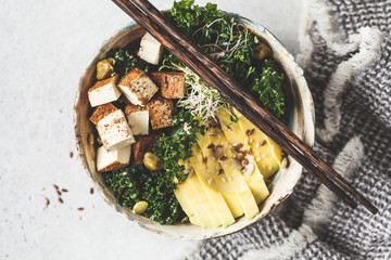 Vegan salad with smoked tofu, kale, avocado and sprouts in bowl.