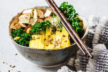 Vegan salad with smoked tofu, kale, avocado and sprouts in bowl.