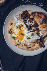Poached eggs with runny egg yolk on a hummus with sautéed mushrooms, toasted bread anf herbs 