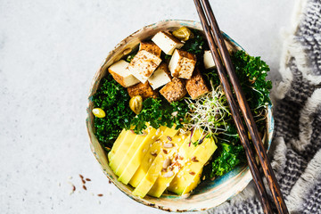 Vegan salad with smoked tofu, kale, avocado and sprouts in bowl.