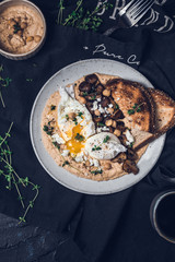 Poached eggs with runny egg yolk on a hummus with sautéed mushrooms, toasted bread anf herbs 