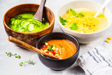 Three different vegetable cream soups in bowls on gray background. Corn, cucumber and gazpacho soups.