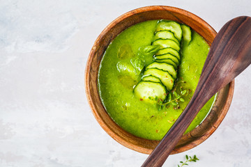 Vegan cold cucumber cream soup in wooden bowl on a gray background.
